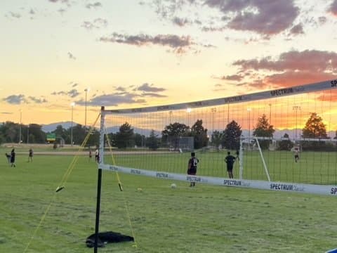 A Spectrum Classic volleyball net set up on the grass at Veterans Park in Denver at sunset